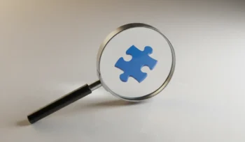 Magnifying glass highlighting a lone blue puzzle piece on a neutral background, symbolizing a missed question in competitor research.