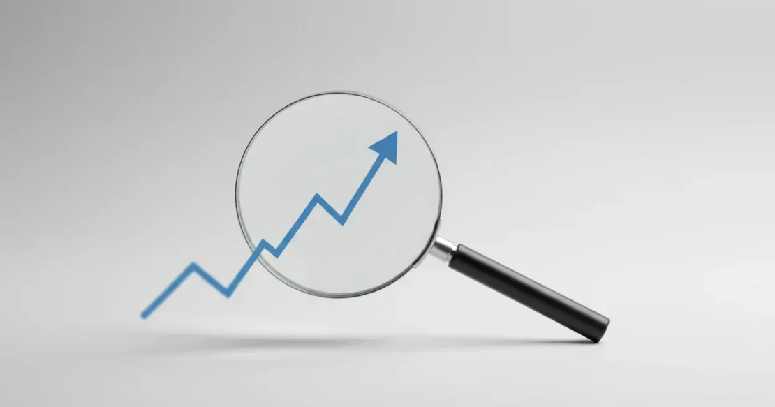 Magnifying glass revealing a sharp upward trend line on a soft, neutral background.